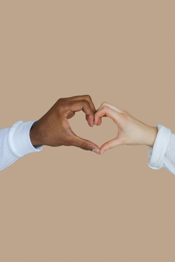 Interracial hands creating a heart shape on brown background, symbolizing love and unity.